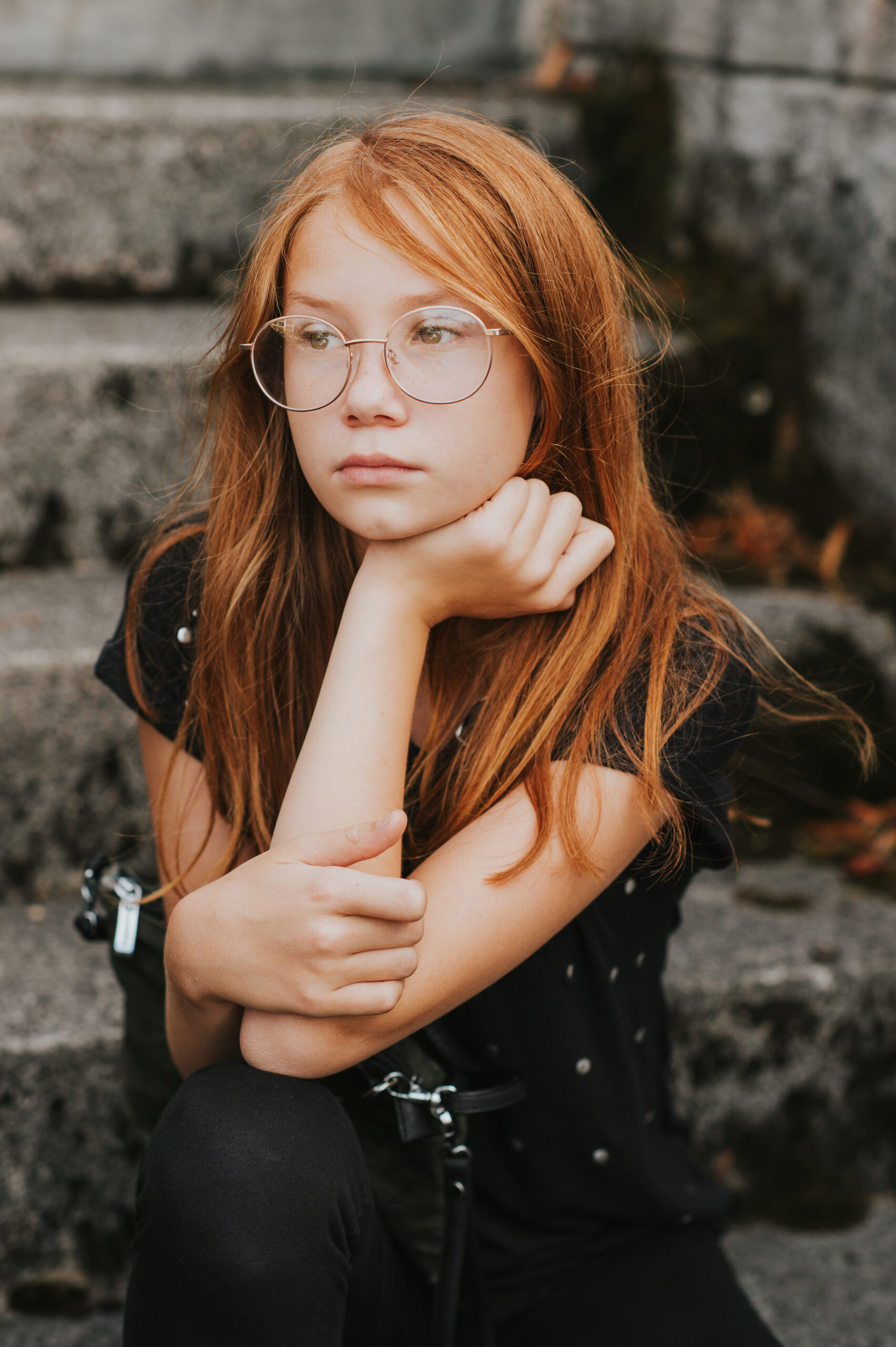 young female with red hair and glasses staring off to the side with chin resting on hand